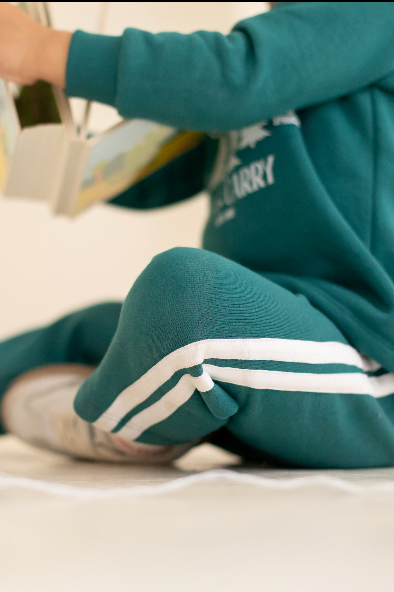 Person wearing a teal tracksuit with white stripes sitting on the floor.