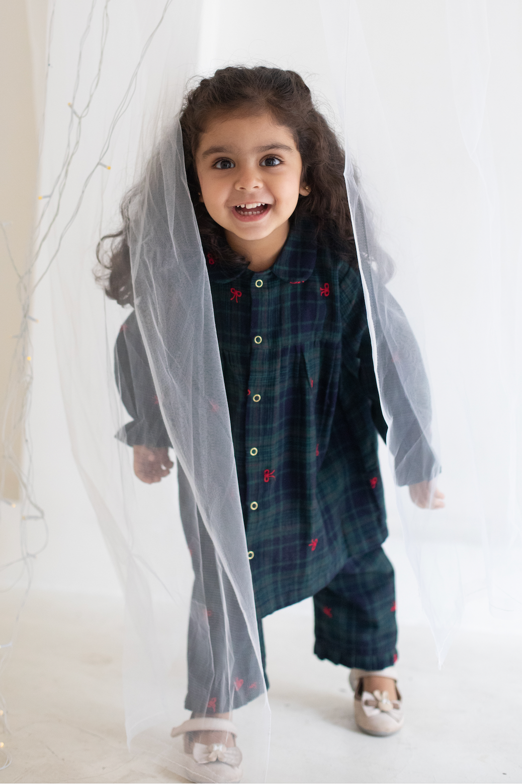 Child wearing a dark plaid outfit with a sheer overlay against a white background