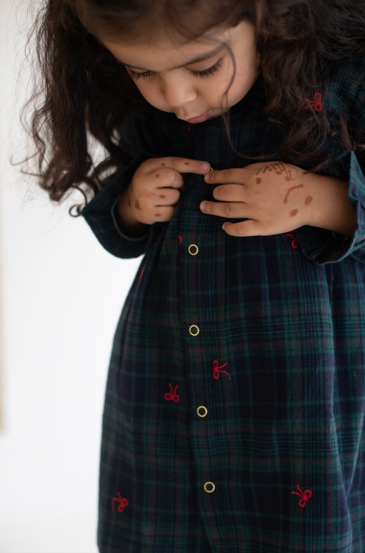 Child wearing a dark plaid dress with red embroidery on a white background
