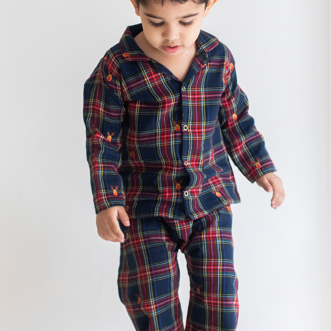 Child wearing a navy and red plaid pajama set on a white background