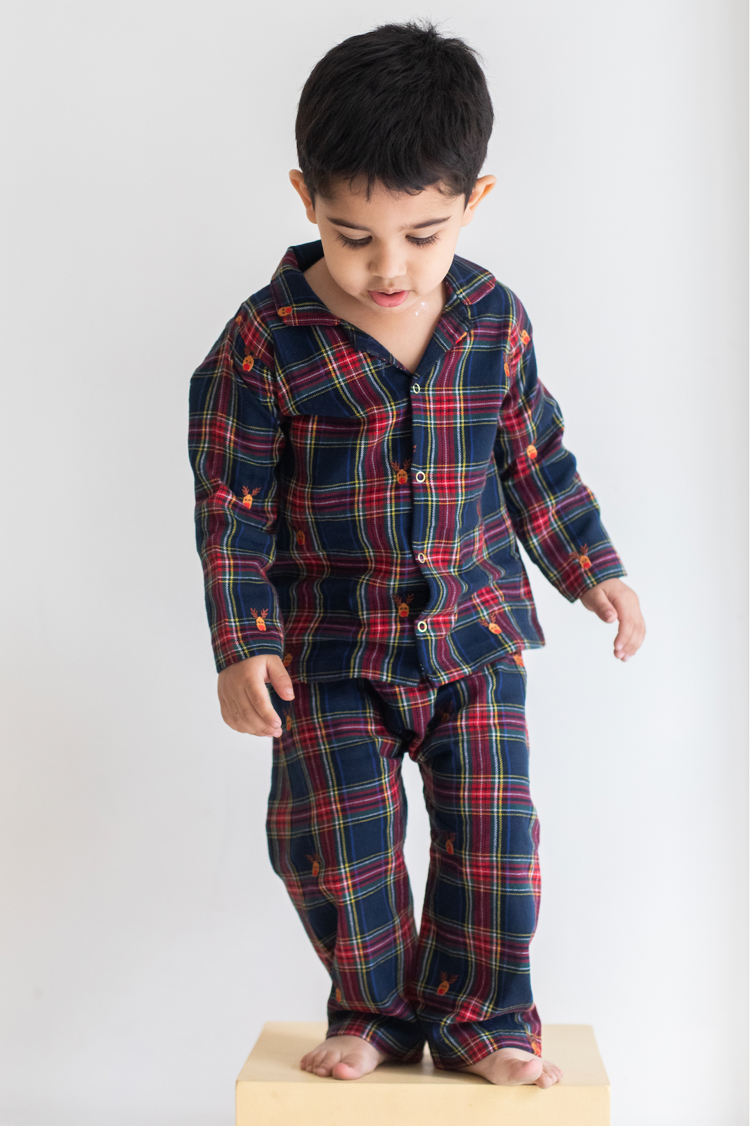 Child wearing a navy and red plaid pajama set on a white background