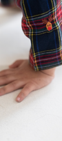 Child's hand and part of a plaid garment on a white surface