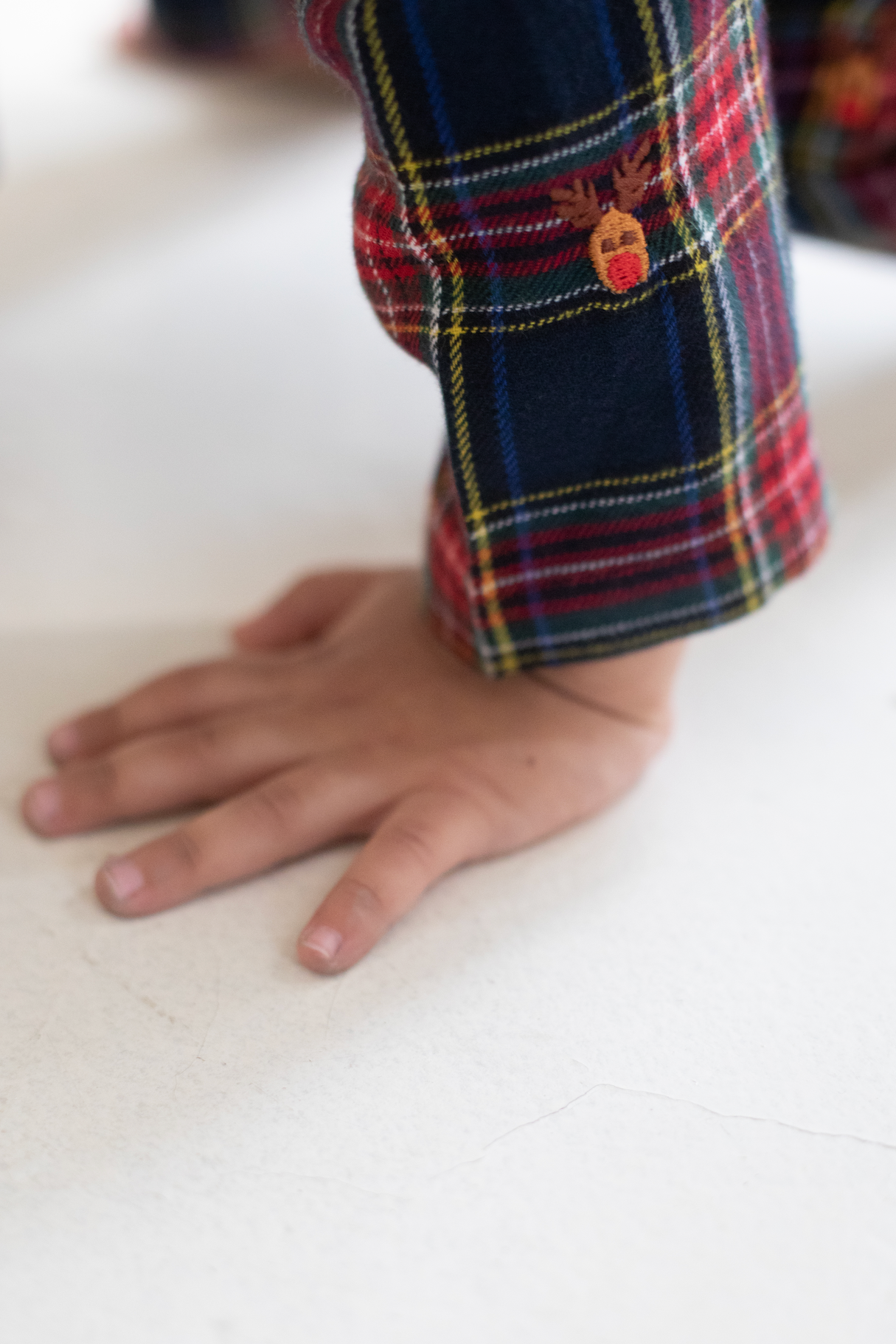 Child's hand and part of a plaid garment on a white surface
