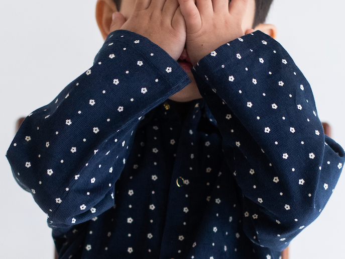 Child wearing a navy blue JACKET shirt sitting on a chair with a white background