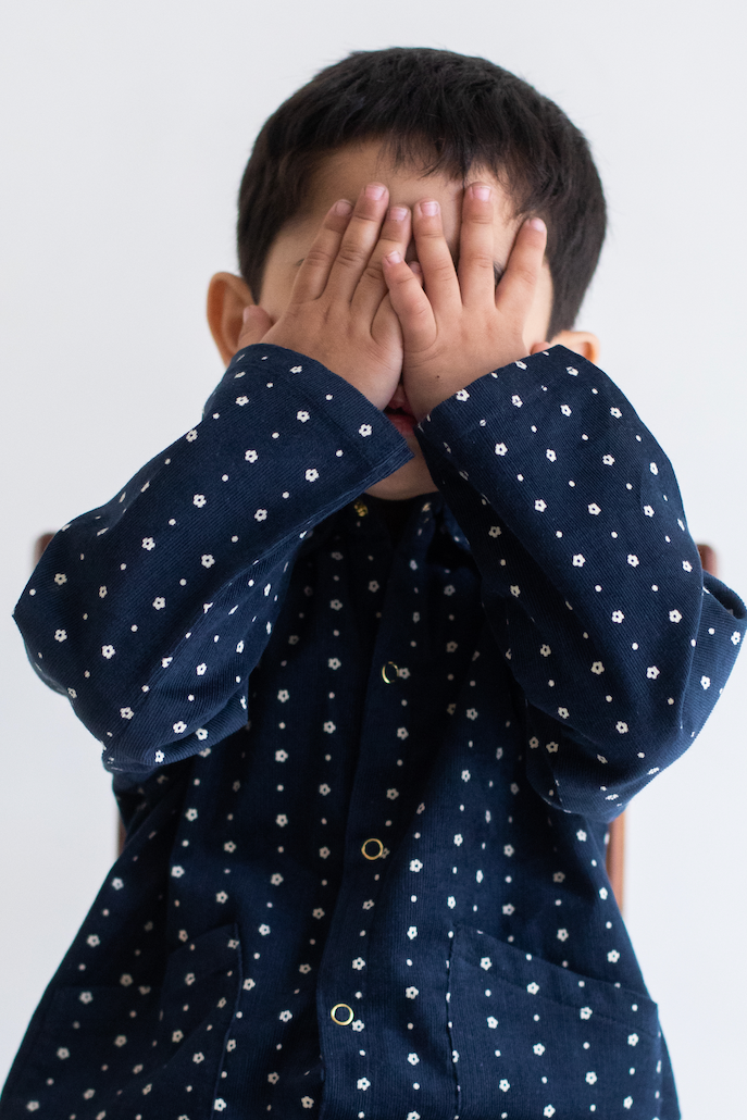 Child wearing a navy blue JACKET shirt sitting on a chair with a white background