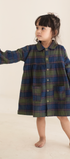 Child wearing a plaid dress standing against a plain background