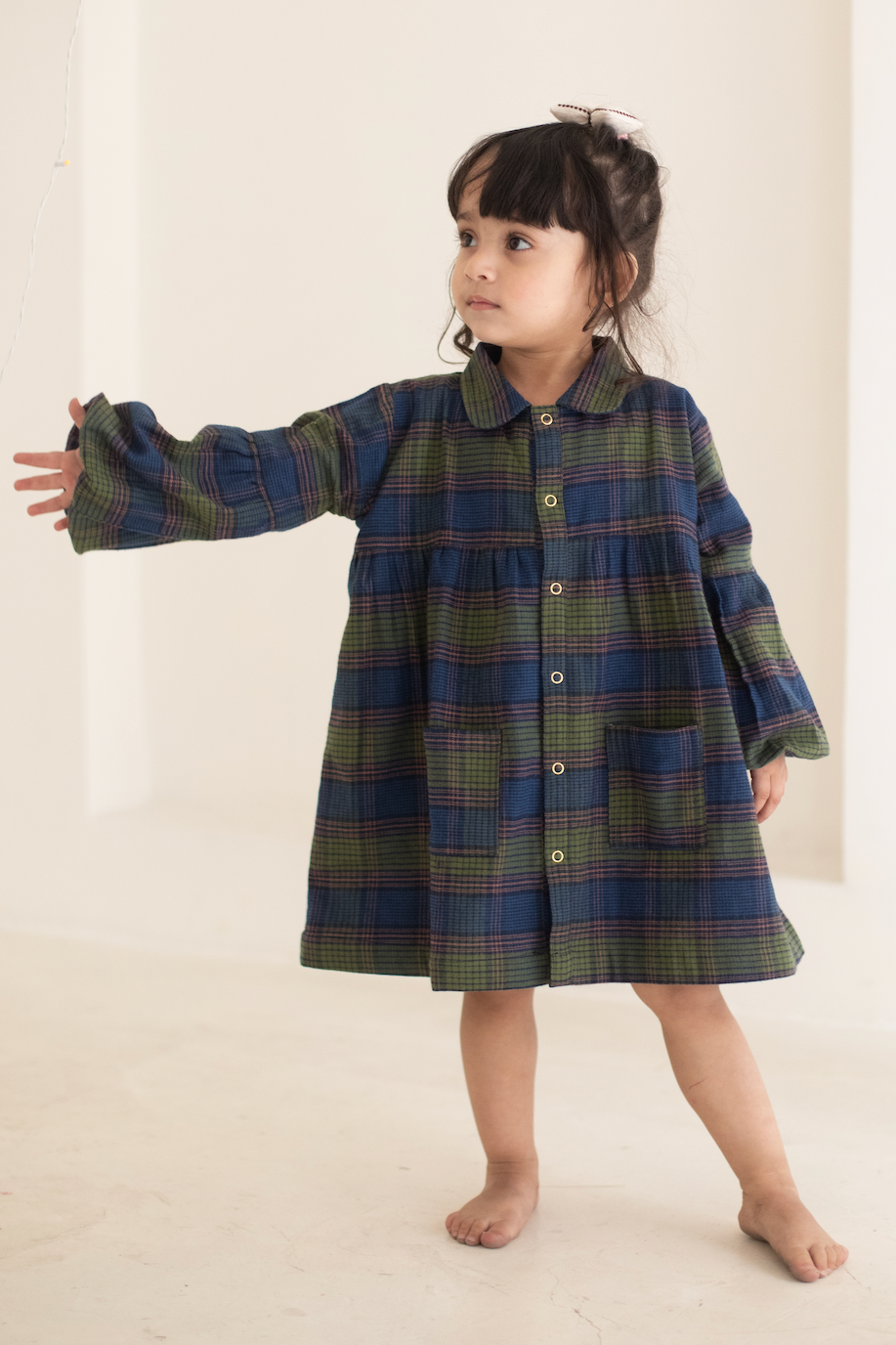 Child wearing a plaid dress standing against a plain background