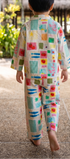 A child seen from behind walking barefoot on a tropical resort path, wearing a matching two-piece pajama set with a colorful patchwork print on a cream background.