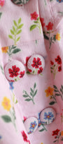 Close-up of a pink fabric with floral patterns and buttons.